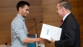 Mitarbeiter übergibt Studierendem eine DAAD-Urkunde